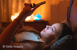 Image of teen girl looking at her phone in bed